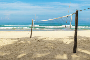 Beach volleyball court with net on sandy tropical shore under blue sky