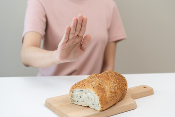 Gluten allergy, asian young woman hand push out, refusing to eat white bread loaf on board in...