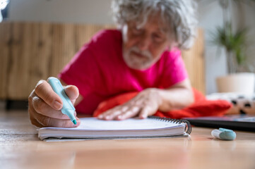 Senior man writing or drawing in notebook on floor at home