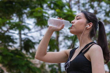 Portrait of beautiful Asian runner drinking water from plastic bottle because she feels tired from run and wants take break drink water. Beautiful Asian woman taking break drink water after tiring run