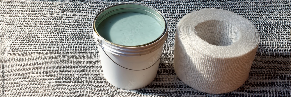 Aufkleber Roll of Fiberglass Mesh Next to a Bucket of Glue for Construction and Repair Projects in a Workshop Setting