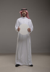 Arab man and boy wearing traditional Saudi thobe, holding a blank round sign and pointing at it with confidence. Concept for advertising, announcements, and marketing content.