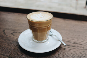 Flat white coffee with latte art in glass cup on wooden table