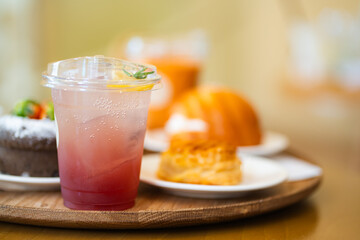 Close up glass of ice blueberry juice with soda on wooden tray with blurred dessert background at cafe.