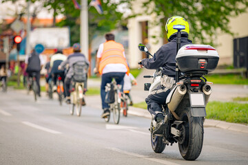 Fototapeta premium Police officer on motorcycle secures group of cyclists on city road, street, asphalt