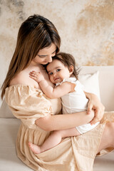 a mother with a baby, a young mom gently hugs and kisses her newborn baby, holding him in her arms, maternal love and care, a mother having fun with her child at home