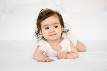 Fototapeta premium A baby crawls on a white bed at home, a smiling toddler in close-up on the bed