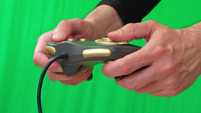 A close-up shot of hands actively holding and operating a black video game controller with gold accents against a vibrant green screen background