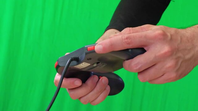A close-up shot of hands actively holding and operating a black video game controller with gold accents against a vibrant green screen background
