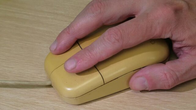 A close-up shot of a hand holding a unique wooden computer mouse with two buttons and a scroll wheel, set against a neutral background