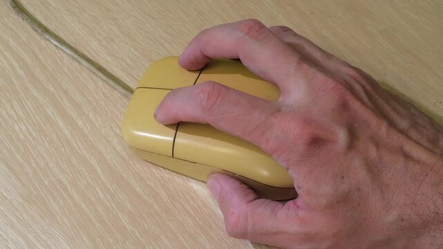 A close-up shot of a hand holding a unique wooden computer mouse with two buttons and a scroll wheel, set against a neutral background
