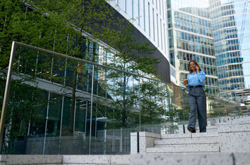 Confident businesswoman walking downstairs with coffee and phone