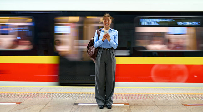 Young woman using smartphone on metro platform with moving train