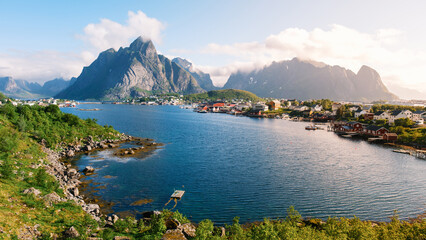 Fototapeta premium Majestic mountains rise above a tranquil fjord in Norway, with quaint fishing cabins nestled along the shoreline. Reine Lofoten Norway