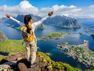 A person stands triumphantly at the edge of a cliff, arms outstretched, reveling in the breathtaking beauty of Lofoten Islands in Norway. © Fokke Baarssen