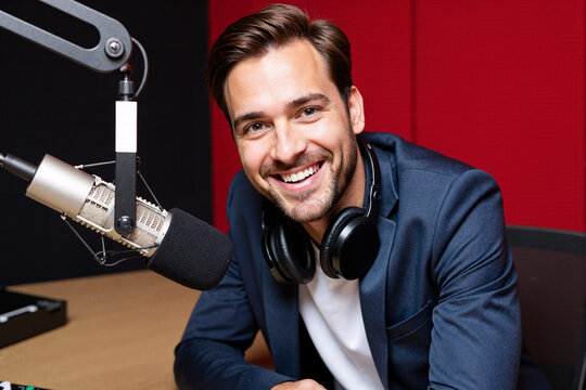 male radio host, podcaster, or broadcaster with headphones smiles confidently into a professional microphone in a recording studio with soundproofing, embodying communication, media, entertainment