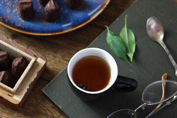 Black tea in a mug on a book on the table, truffle candies lying nearby