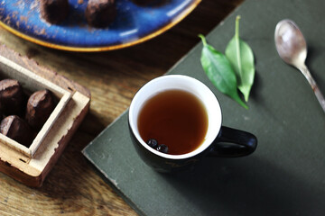 Black tea in a mug on a book on the table, truffle candies lying nearby