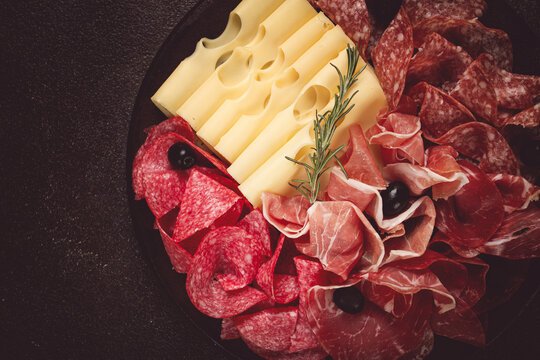 Cold cuts, appetizer, prosciutto, salami and ham, with maasdam cheese and olives, on a round plate, breakfast, top view, close-up, deserted