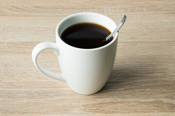 Obraz premium 45-Degree Shot of Coffee-Filled Cup with Spoon on Wooden Table and Light Background