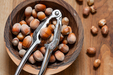 Whole raw hazelnuts in a wooden bowl with a nutcracker on a wooden background.