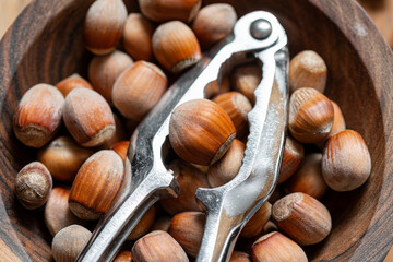 Whole raw hazelnuts in a wooden bowl with a nutcracker on a wooden background.