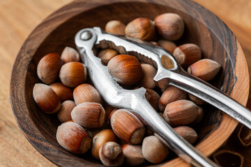 Whole raw hazelnuts in a wooden bowl with a nutcracker on a wooden background.