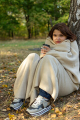 A woman in a blanket sits under a tree with a coffee cup