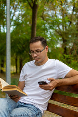 A man is on a bench reading and checking his phone