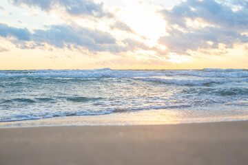Golden sunlight shining through clouds over calm ocean with soft waves lapping at sandy beach