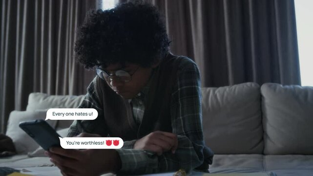 Medium shot with VFX video effects of depressed teenage African American boy, wearing geeky eyeglasses, looking at abusive, violent messages from bullies on social media, appearing around him