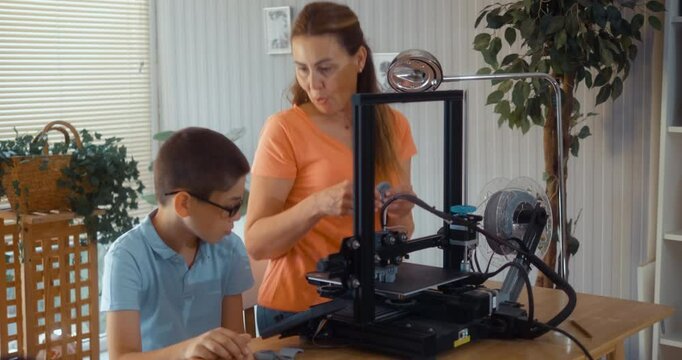 Mother is visiting her teenage son working on a 3D printer at home.