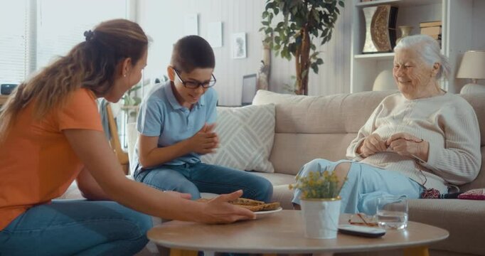 A happy multi-generational family gathers in the living room to eat a freshly baked pie. Excited boy enjoying eating pie with mother and grandmother at home
