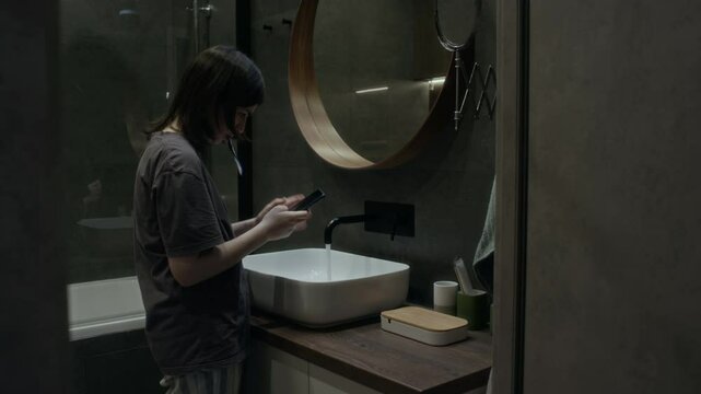 Medium full side shot with VFX effects of anxious young girl standing in bathroom, brushing teeth while scrolling social media, receiving malicious messages and threats from online stalker