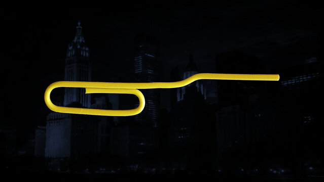 A yellow paper clip deformed by flattening one end. Close-up, black background.