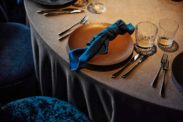A beautifully set dining table with a sophisticated and elegant ambiance. The table is adorned with textured gold plates, polished silverware (forks and knives), and clear glassware, creating a luxuri