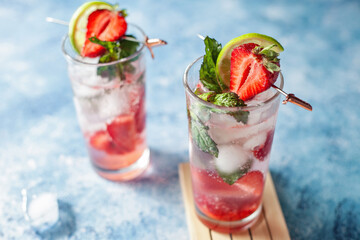 A vibrant strawberry Mojito cocktail or mocktail with fresh lime, mint, and ripe strawberries, on blue background, for a cool, tropical party feel. Refreshing, colorful and sparkling