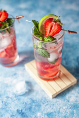 A vibrant strawberry Mojito cocktail or mocktail with fresh lime, mint, and ripe strawberries, on blue background, for a cool, tropical party feel. Refreshing, colorful and sparkling