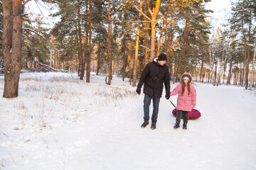 Father and daughter walking with snow tube in the forest