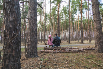 A father and daughter with skateboards are relaxing on a log in the forest.