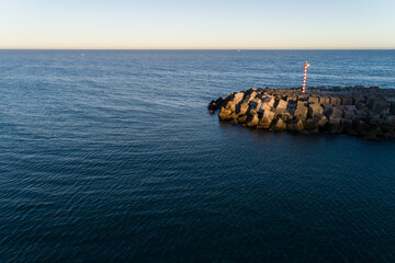 horizontal aerial drone view of a protective breakwater by the calm ocean at sunset