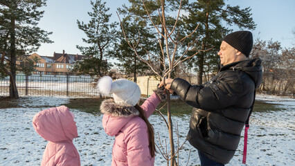 Grandfather walks with his granddaughters after school in the park in sunny winter day