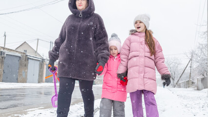 Grandmother and girls walk along a snowy street in winter