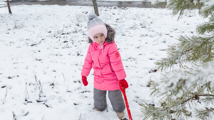 Small girl playing with snow. Child in winter forest on snowy cold day.