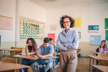 A mature female teacher stand confidently in her elementary classroom