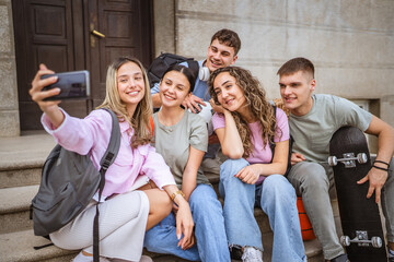 group of happy classmates take a self portrait and sit in front of school
