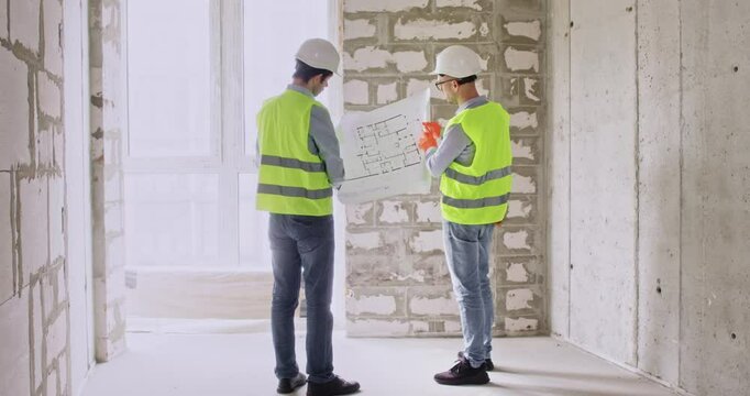 Specialists unfold scheme of apartment and shake hands after concluding deal. Builders discuss renovation process and prepare to begin work in spacious room