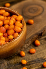 frozen orange sea buckthorn berries in a wooden bowl on the table, defrosting ripe sea buckthorn berries to make a drink, closeup