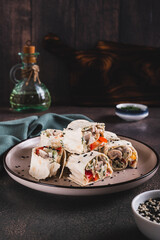 Chicken meat, pepper and cucumber in sauce wrapped in tortilla rolls on a plate vertical view