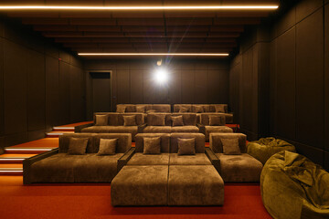Modern cinema room with tiered seating, warm ambient lighting, and soundproofing panels. Comfortable cushioned seats create an intimate and cozy atmosphere for movie viewing.